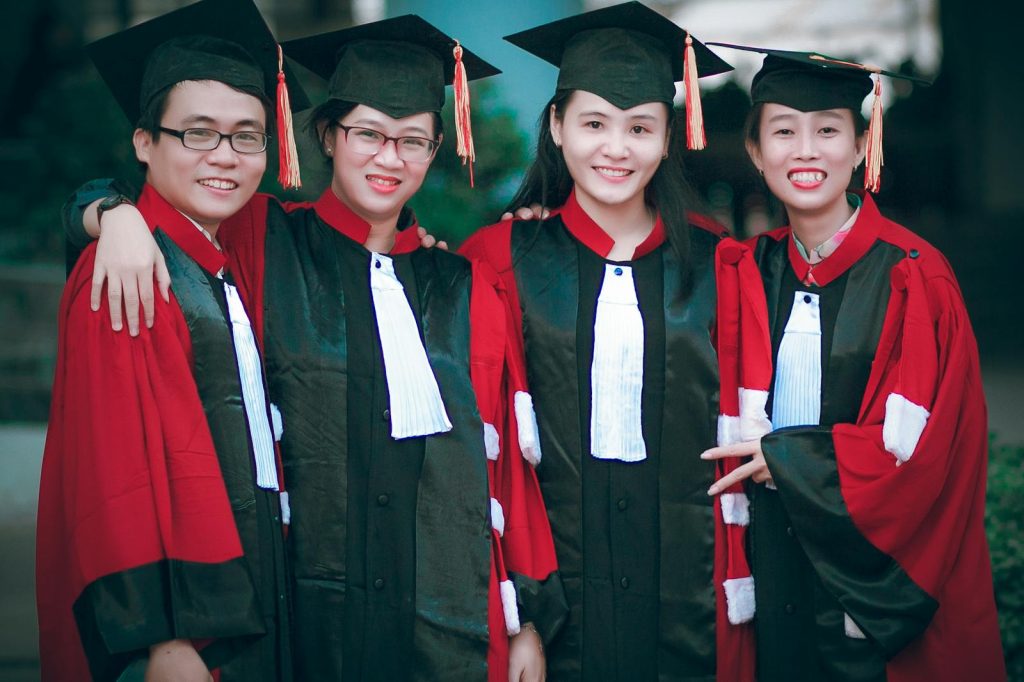 Group of happy graduates in red and black gowns celebrating their success outdoors.