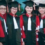 Group of happy graduates in red and black gowns celebrating their success outdoors.
