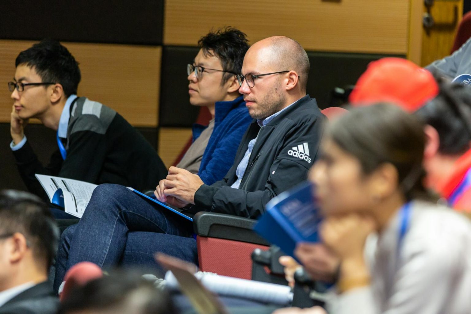 A diverse group of adults attentively listening to a lecture in an indoor conference setting.