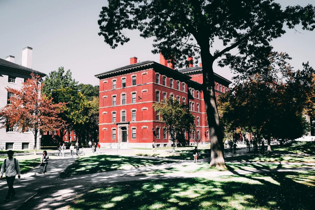 View of a historic red brick university building surrounded by lush trees and walking paths.