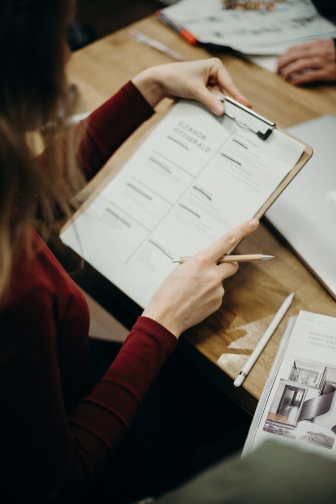 A woman sitting indoors, reviewing documents on a clipboard with focus on detail.