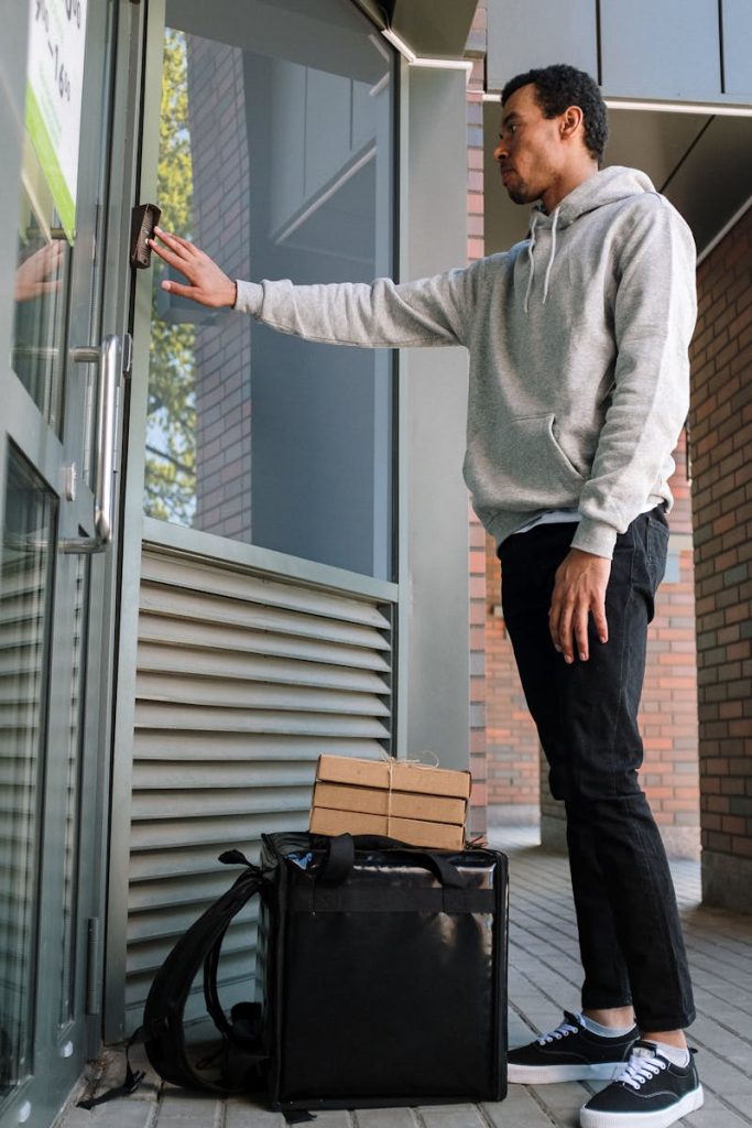 Male courier ringing doorbell for food delivery at modern building entrance.