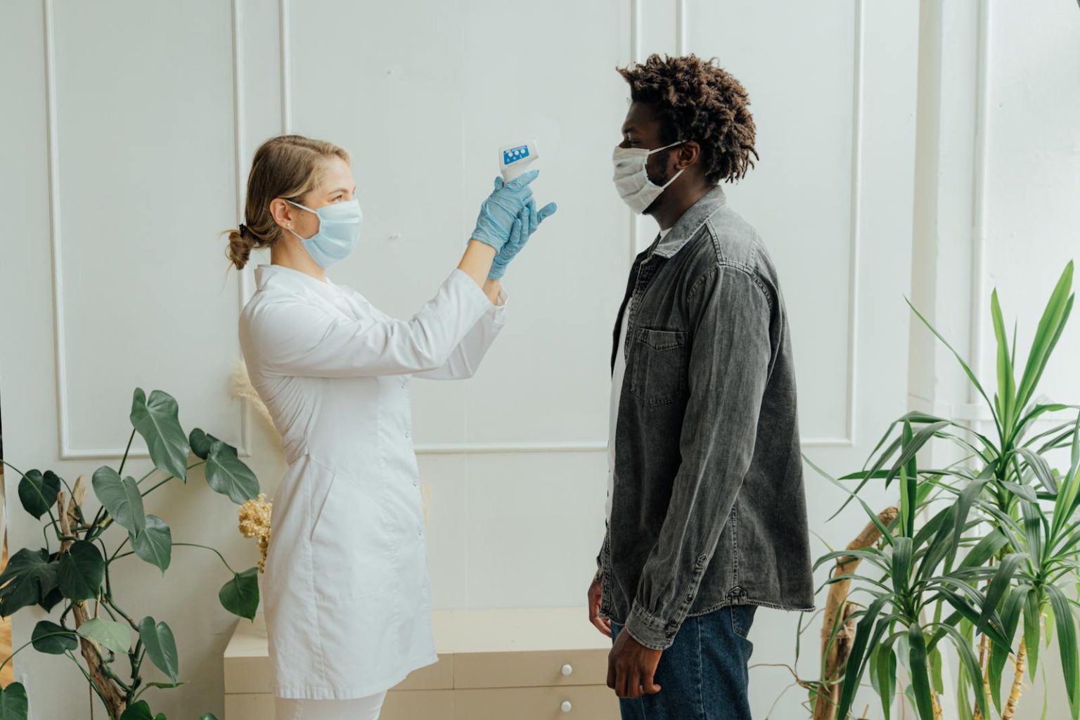 A healthcare professional checks a patient's temperature as part of pandemic protocols in a clinic setting.