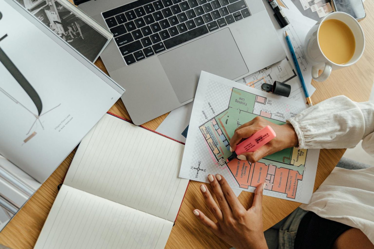 Top view of an architect working on floor plans with a laptop and coffee, highlighting remote work creativity.