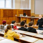 Students engaging with a professor in a university lecture hall, utilizing technology.