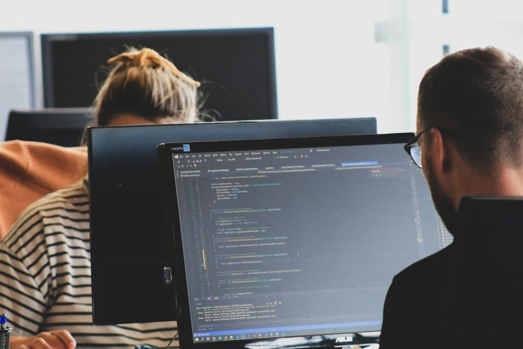 Two colleagues working at computer monitors in an office, illustrating a technology workplace.